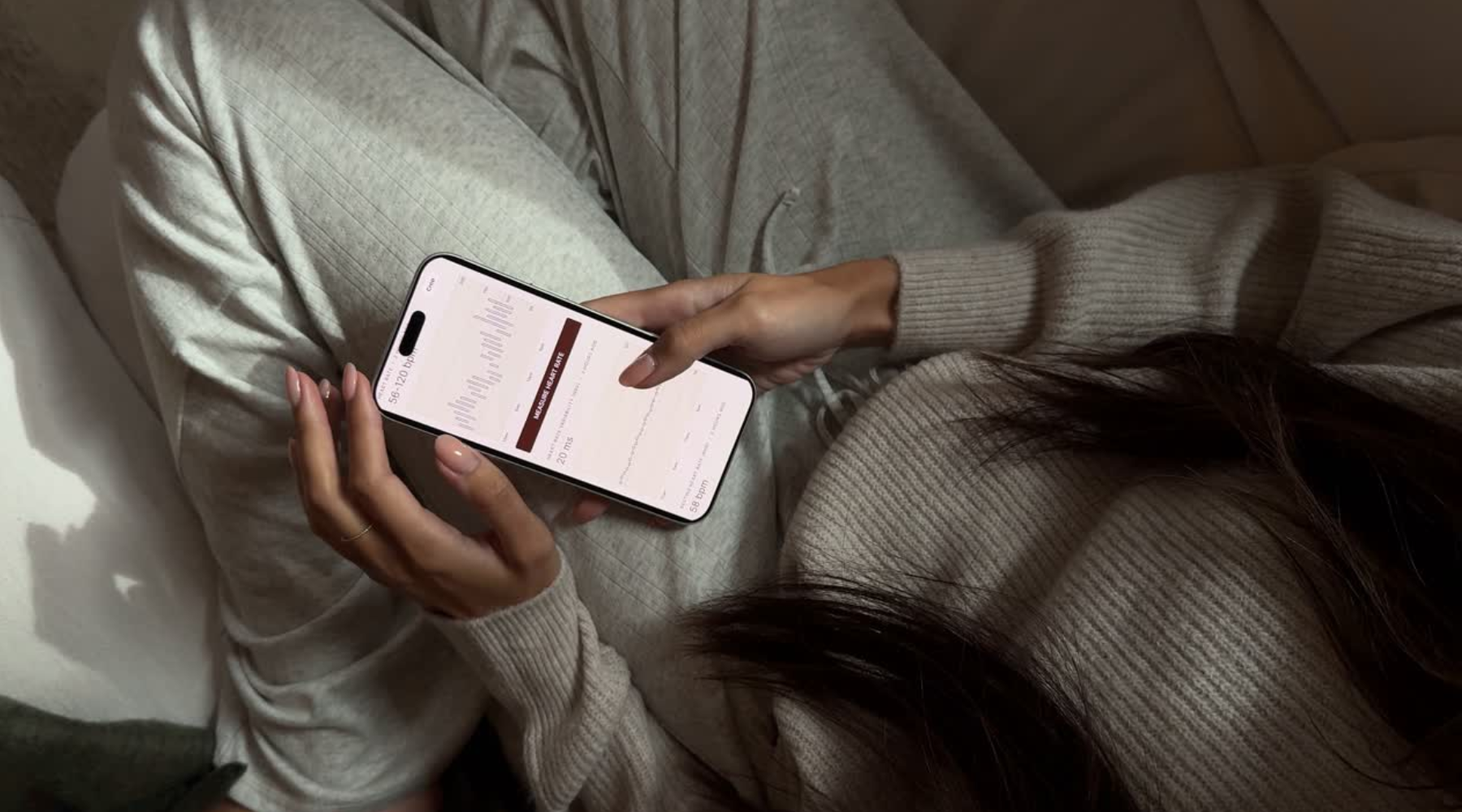 A woman holds a phone, on which she's scrolling through Petal's Heart monitoring in the app.